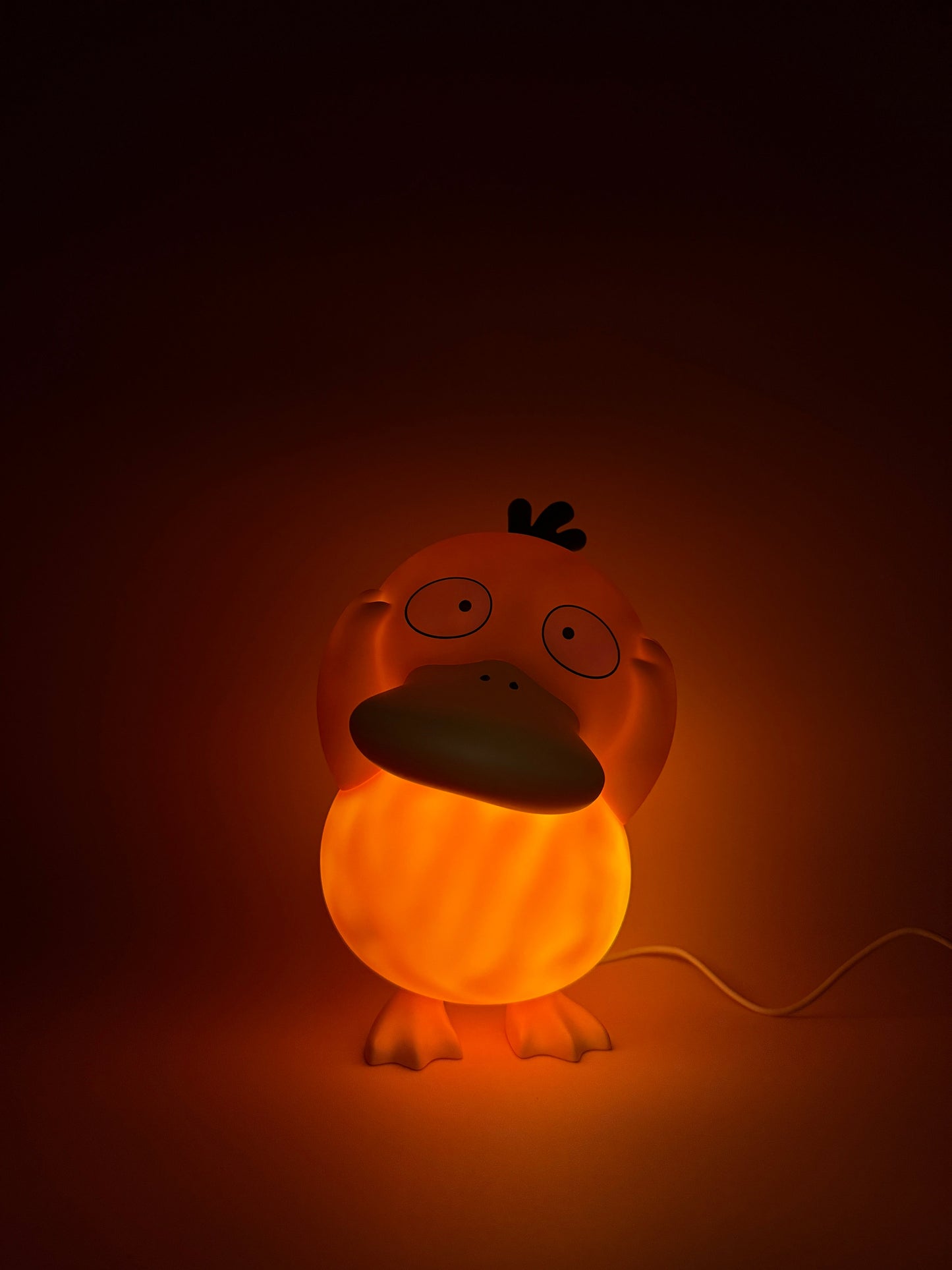 8" Psyduck statue desk lamp with USB cord, glowing warmly, features unique Pokemon design.