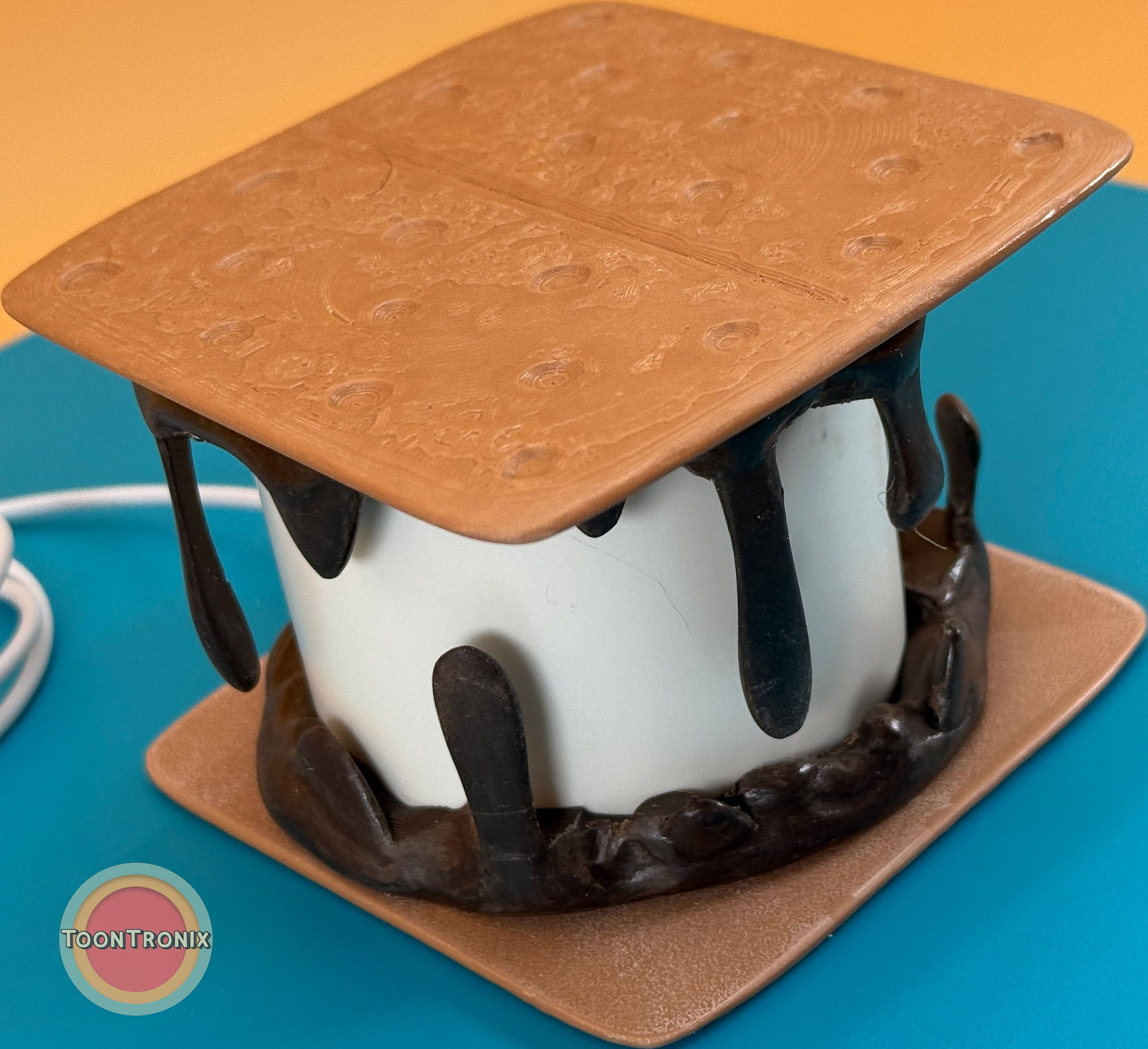 Retro-style smores desk lamp with marshmallow center, chocolate drip details, and graham cracker top and base.