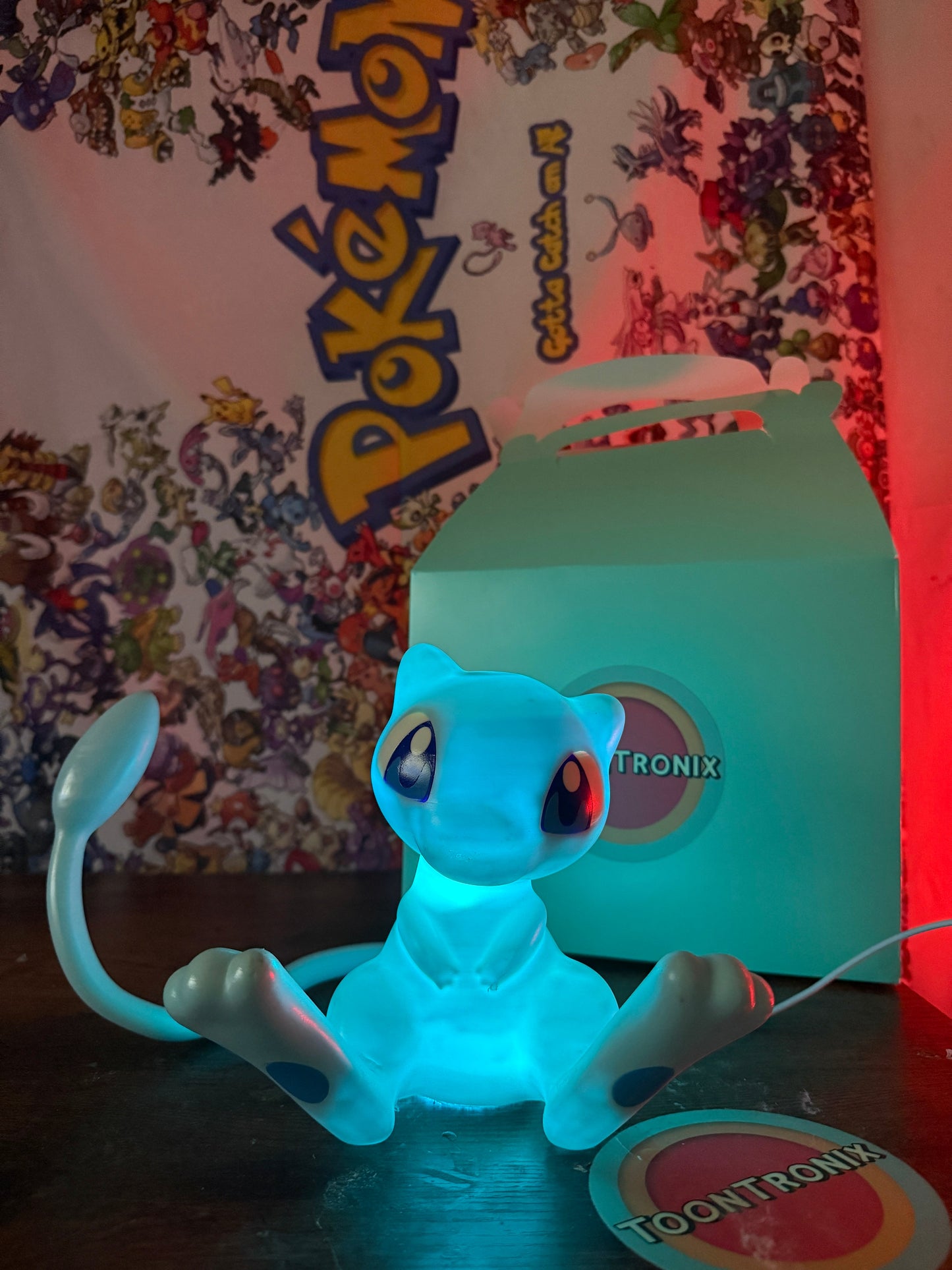 6" tall 11" wide shiny Mew Pokemon LED desk lamp with USB cord glowing blue next to Toontronix packaging
