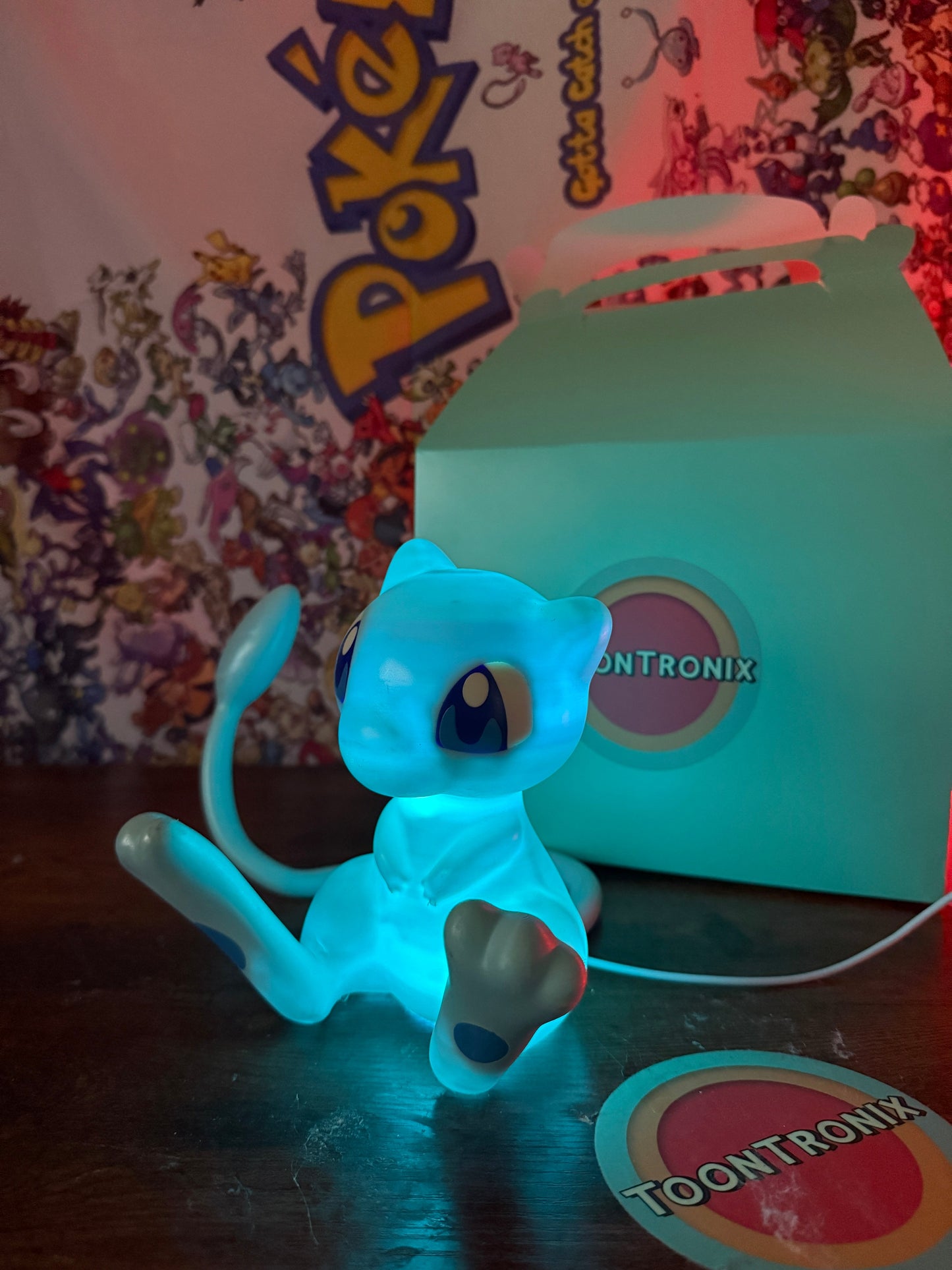 6 inch tall shiny Mew Pokemon statue desk lamp with LED light and built-in USB cord in glowing blue color next to Toontronix box