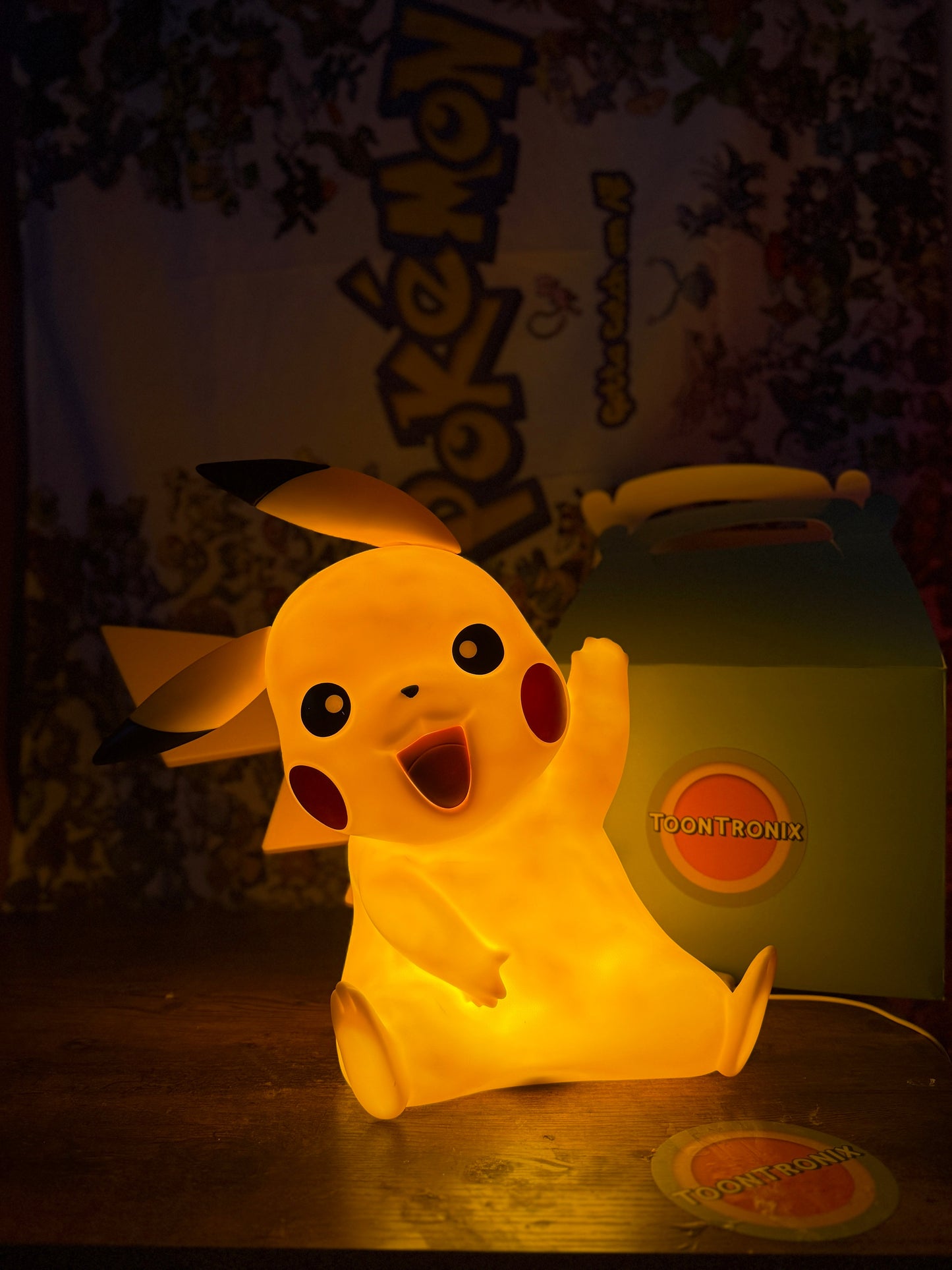 13" Pikachu Large Statue LED USB Desk Lamp glowing warmly on a wooden surface with a Pokemon backdrop and Toontronix box nearby