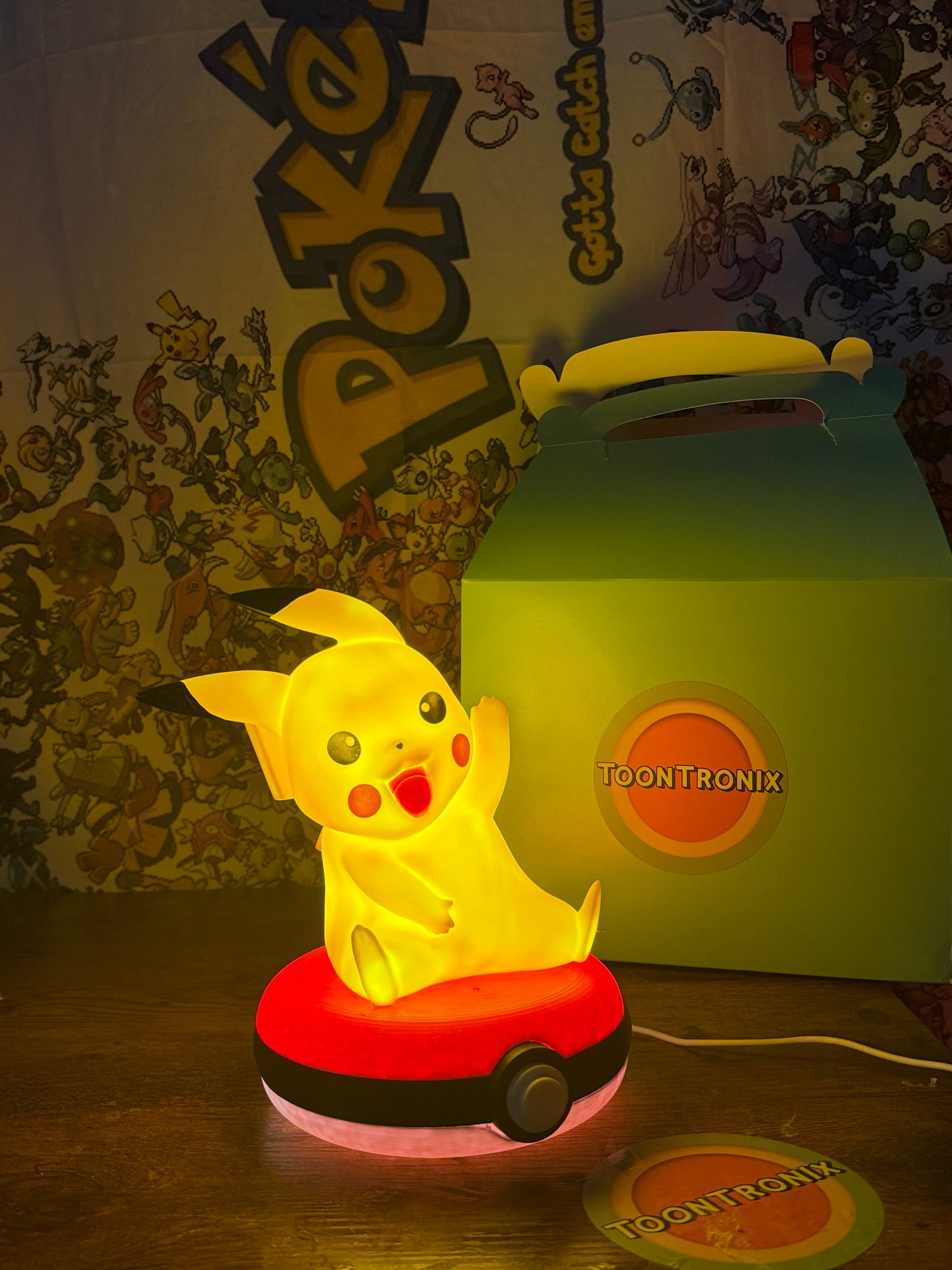 Glowing Pikachu figure sitting on a Pokeball base USB desk lamp with warm yellow light and Pokemon-themed background.