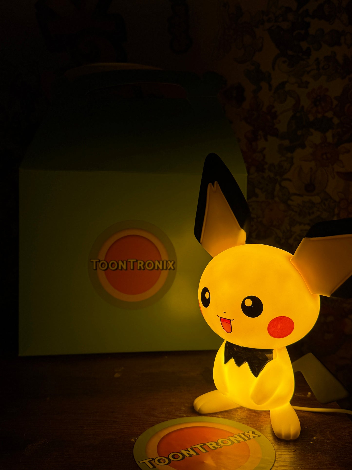 8.5 inch Pichu statue desk lamp with USB light glowing on a wooden surface next to Toontronix packaging