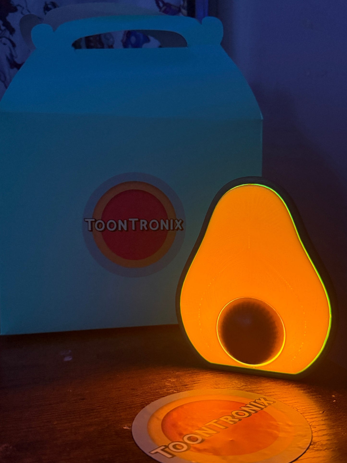 LED avocado desk lamp with USB power glowing orange in front of Toontronix box and sticker