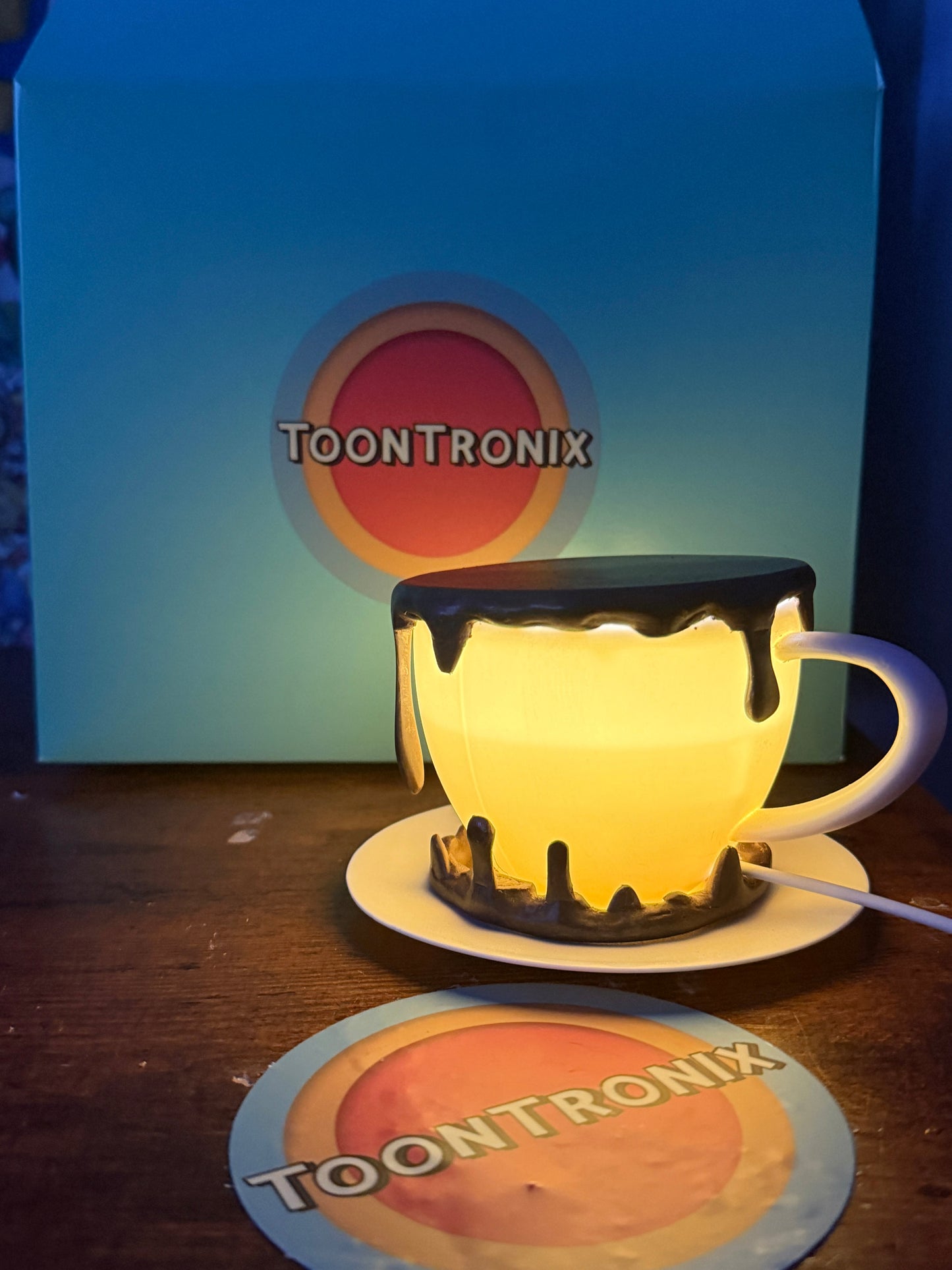 6" or 9" coffee cup desk lamp glowing with warm LED light and dripping paint design on wooden surface with Toontronix packaging in the background
