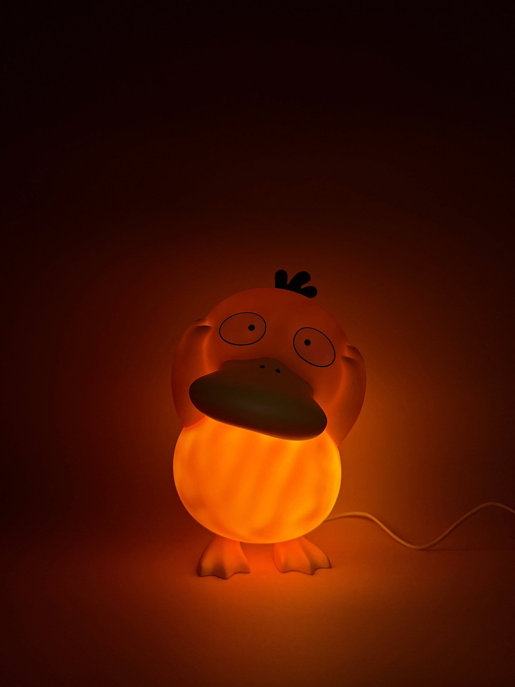 8" Psyduck statue desk lamp with USB cord, glowing warmly, features unique Pokemon design.
