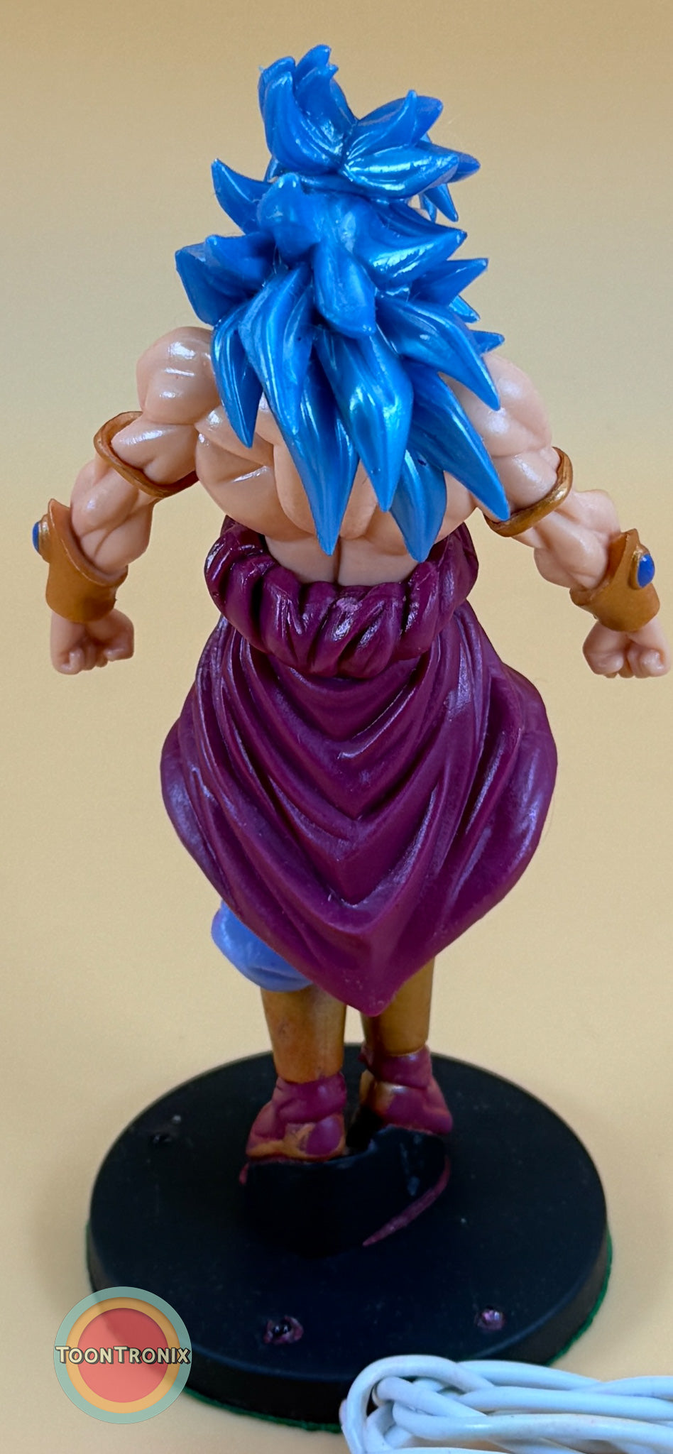 Back view of 7" Dragonball Z Broly statue with blue hair and purple clothing on a black base with USB cord nearby