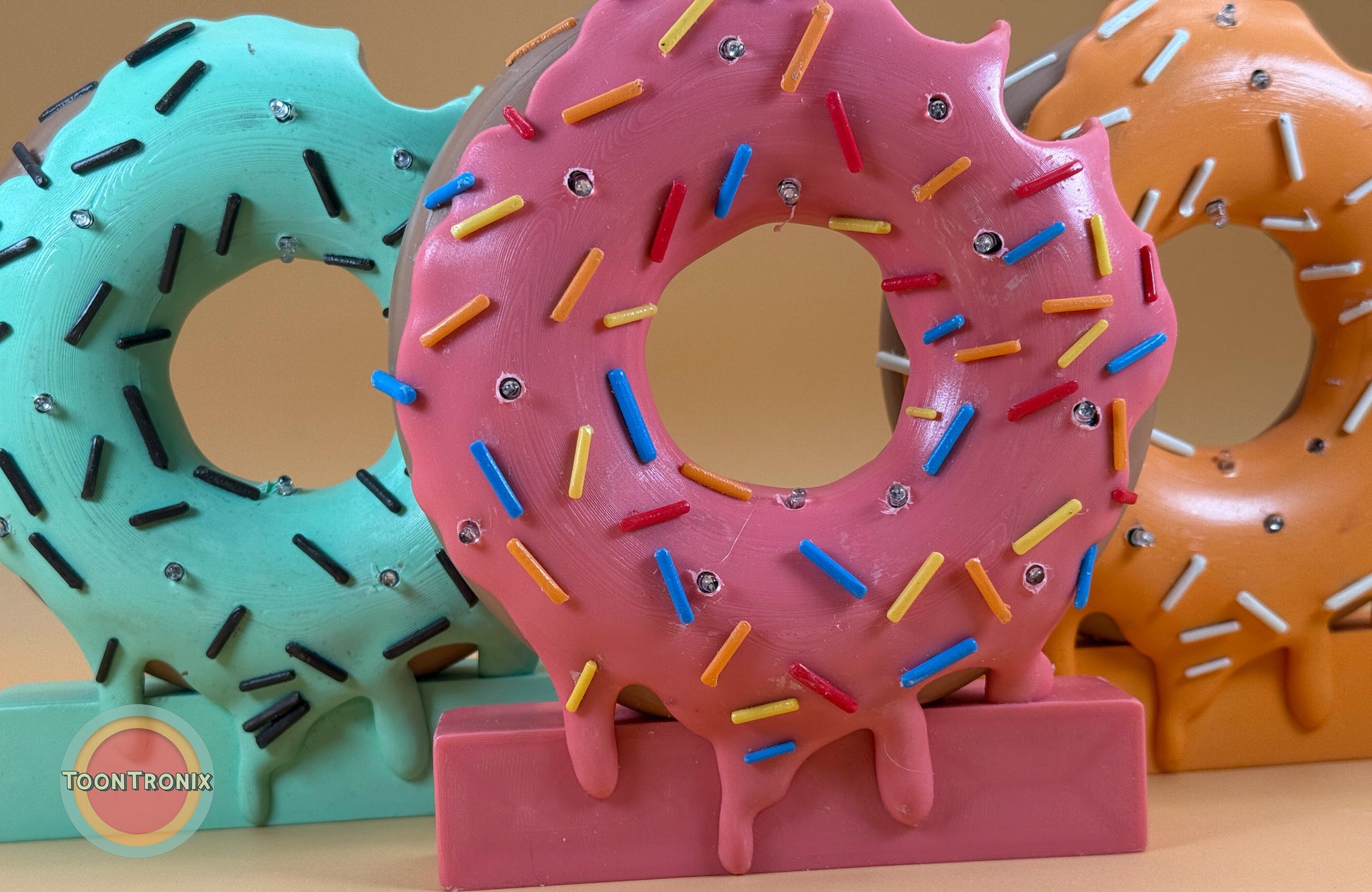 Colorful 6" or 9" donut-shaped desk lamps with sprinkles in retro cartoon style, available in pink, teal, and orange colors.