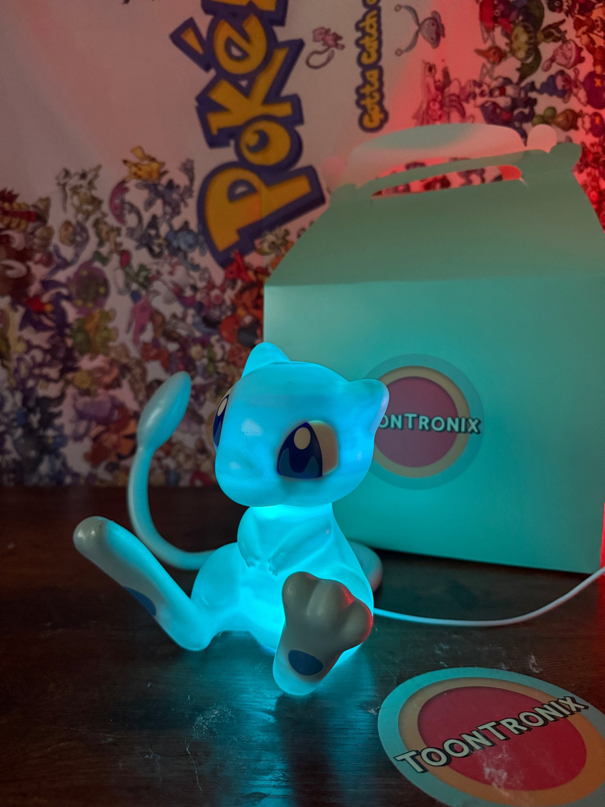 6 inch tall shiny Mew Pokemon statue desk lamp with LED light and built-in USB cord in glowing blue color next to Toontronix box