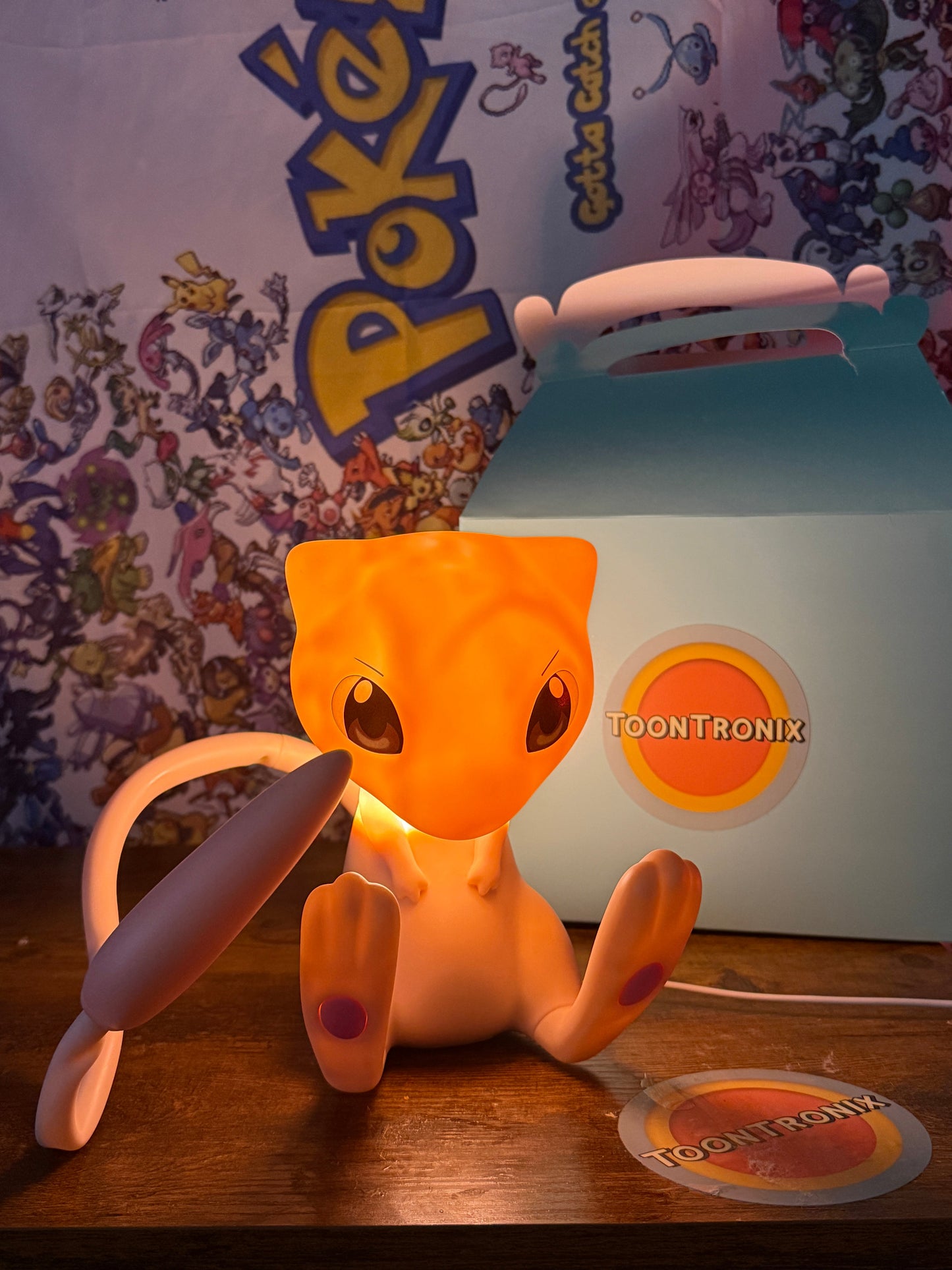7.5” Mew Desk Lamp figure with movable tail and USB cord glowing on wooden surface with Pokemon backdrop and Toontronix packaging