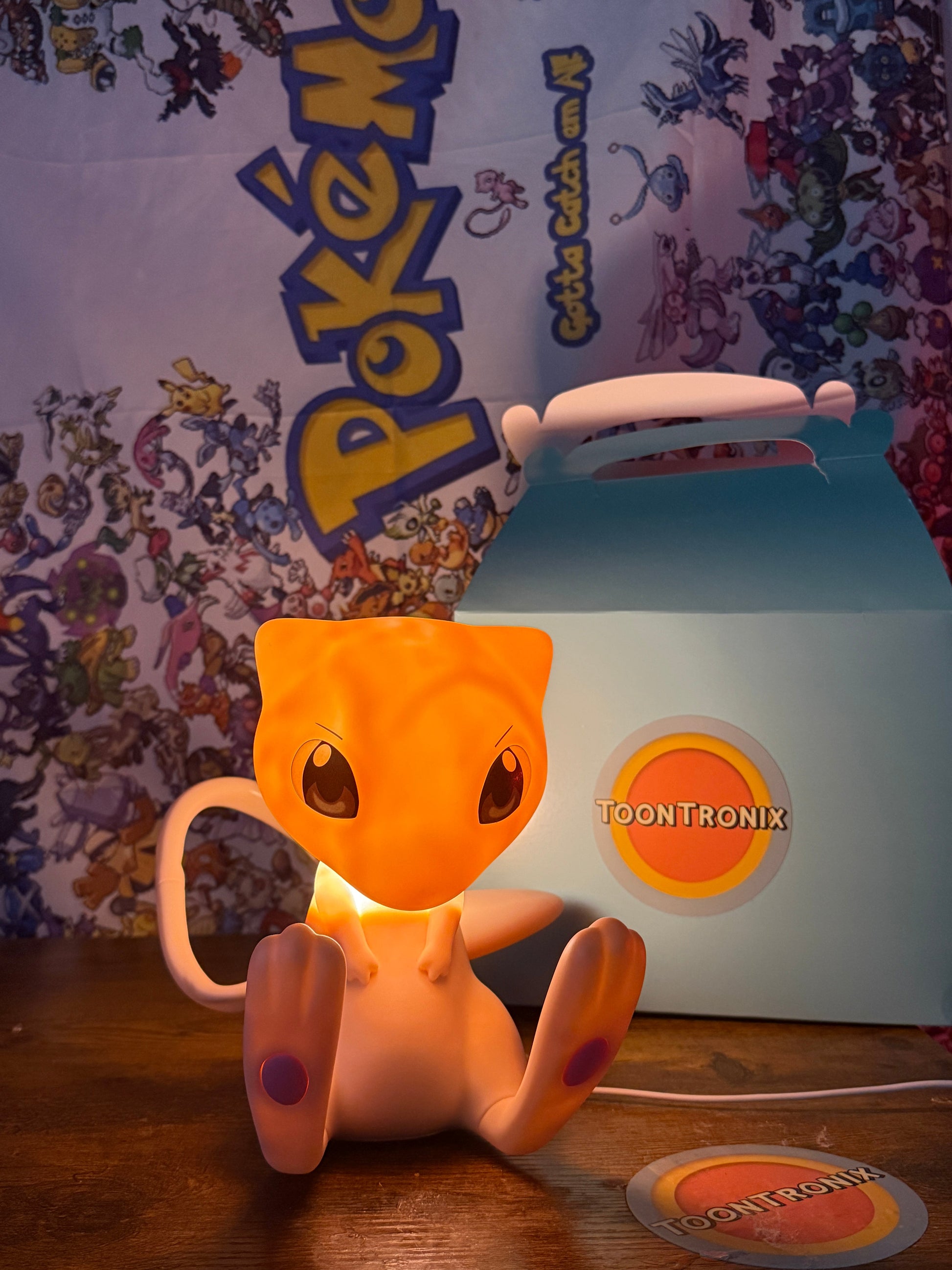 7.5” Mew Desk Lamp with movable tail and built-in USB light glowing on wooden surface with Pokemon background and Toontronix packaging